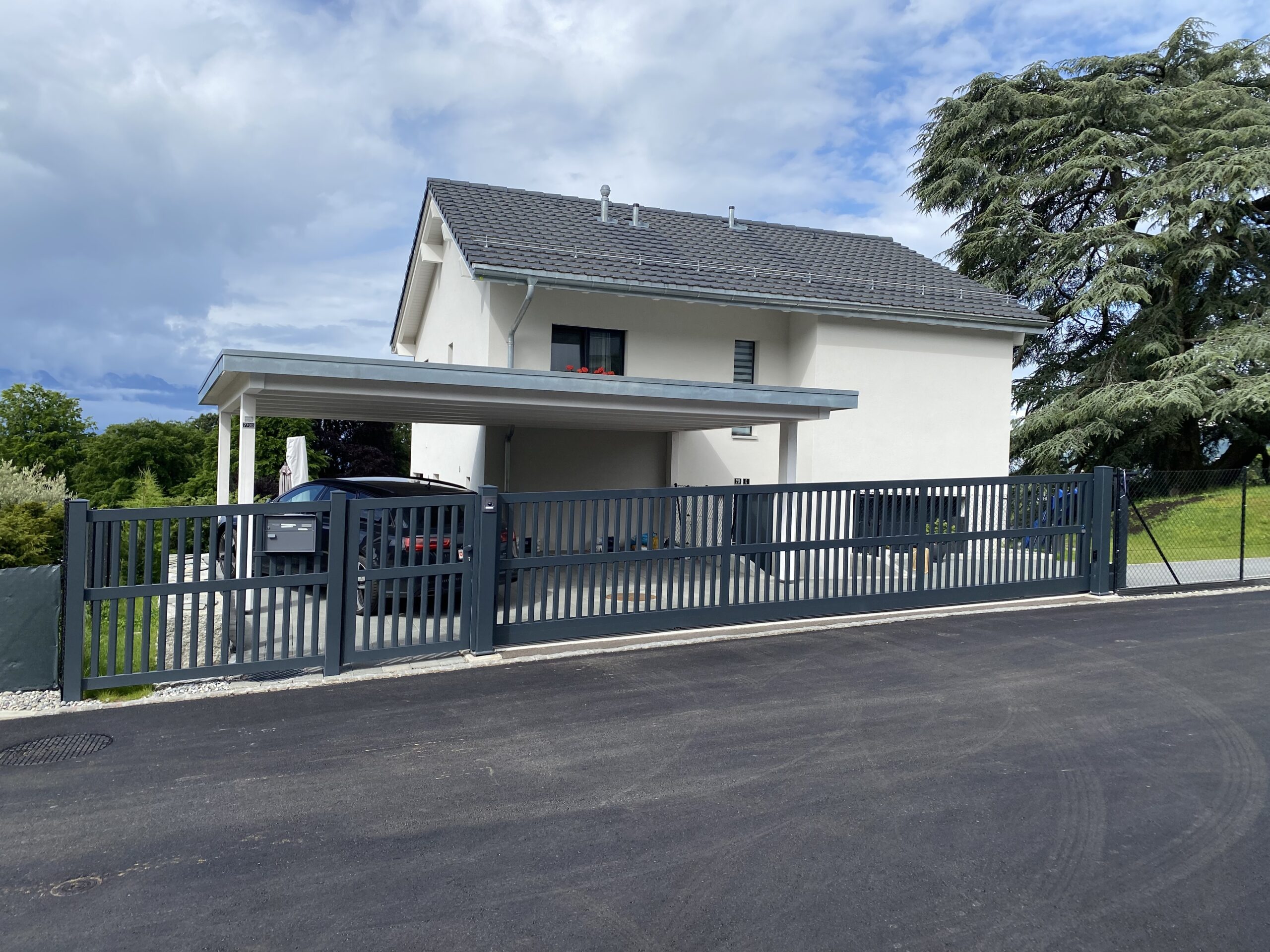 Maison moderne avec portail coulissant, clôture métallique, carport et garde-corps installés par spécialistes suisses d'ouvertures extérieures.
