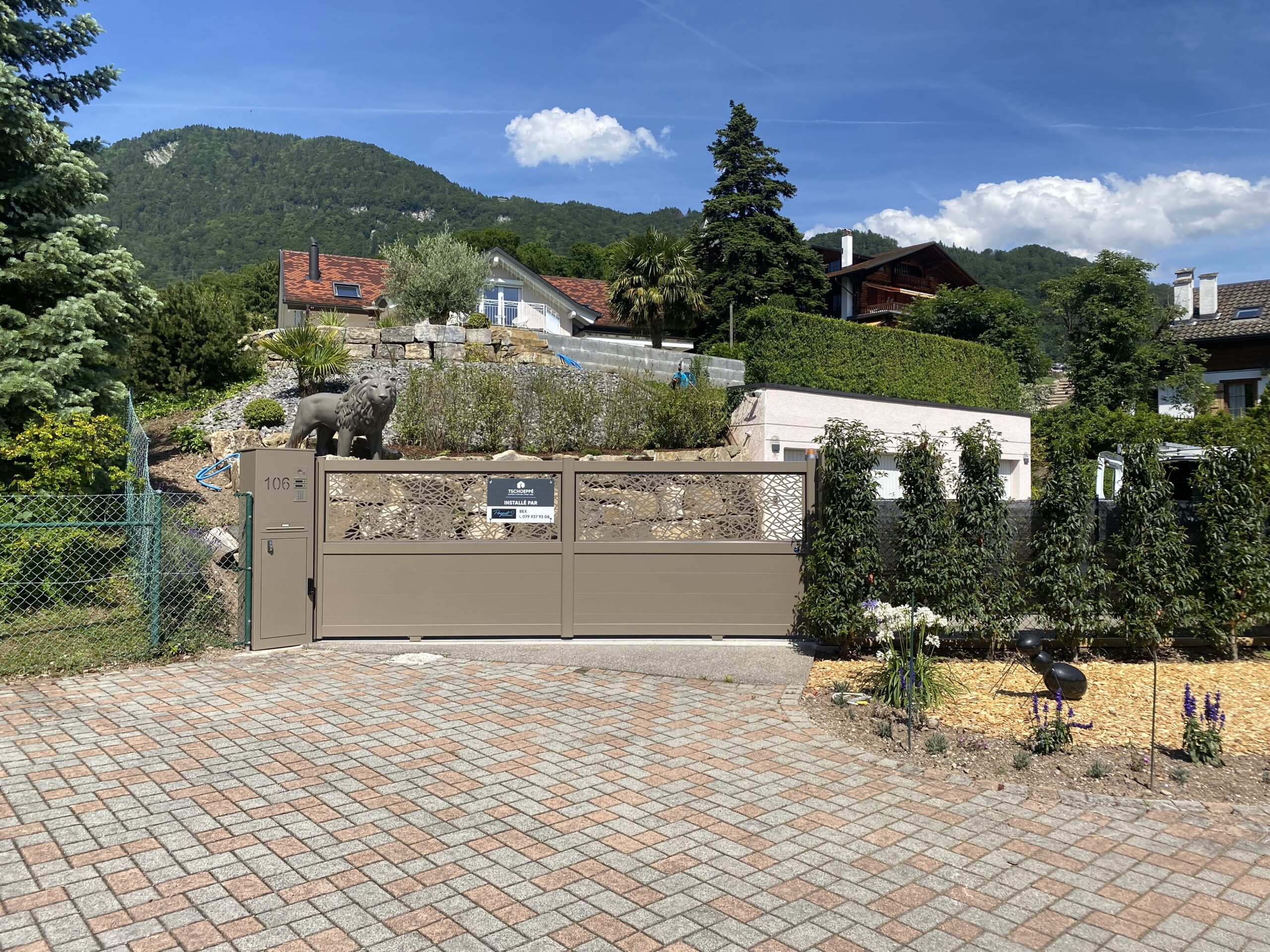 Installation portail moderne suisse, clôture beige, paysagisme, vue montagne.