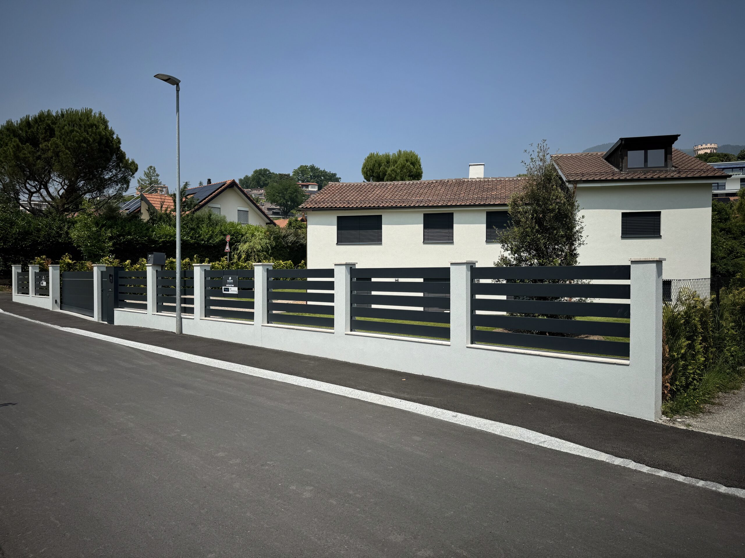 Clôture extérieure moderne installée devant maison suisse, portail motorisé, sécurité.