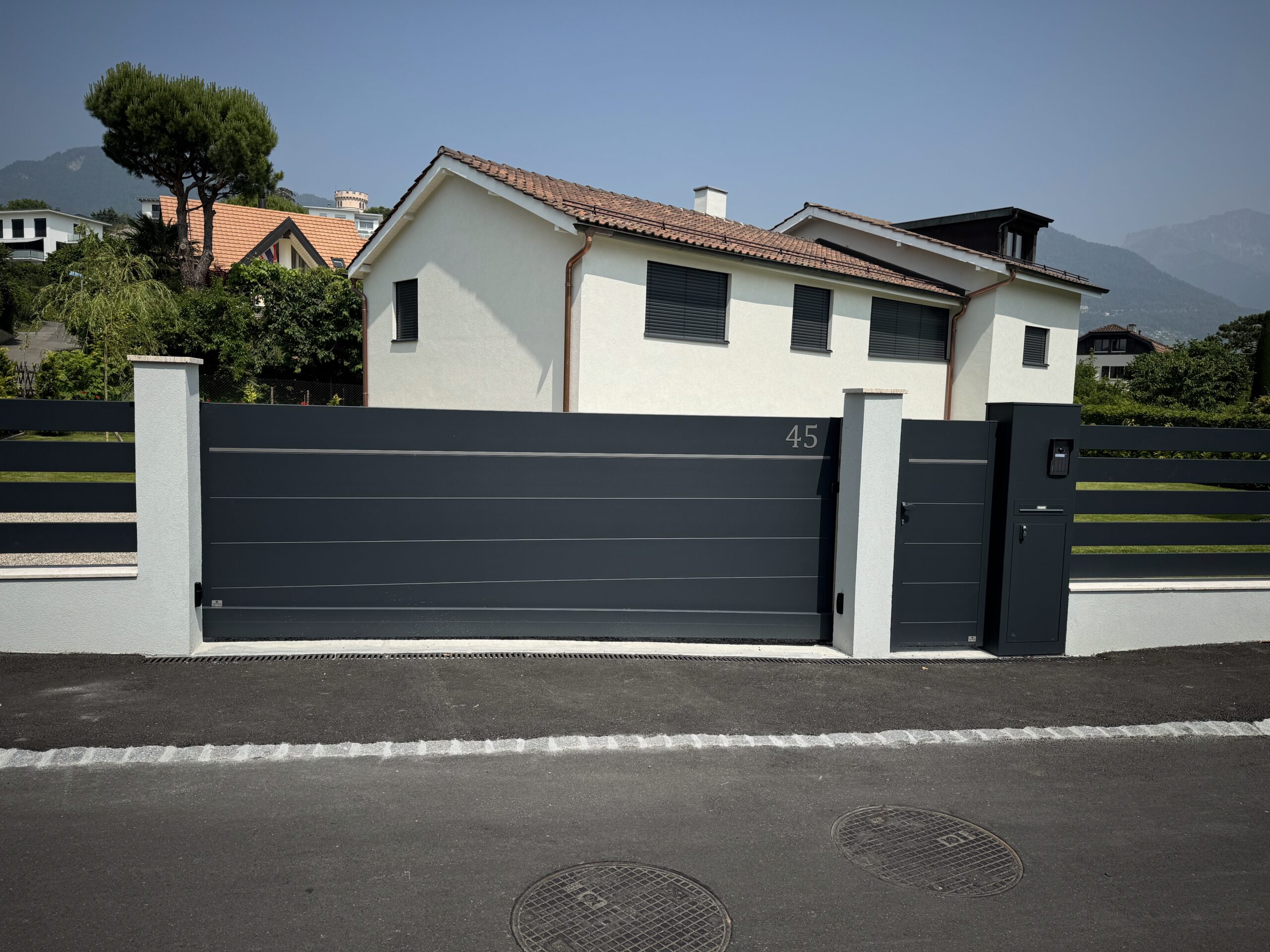 Portail extérieur moderne et clôture installés devant maison suisse contemporaine.