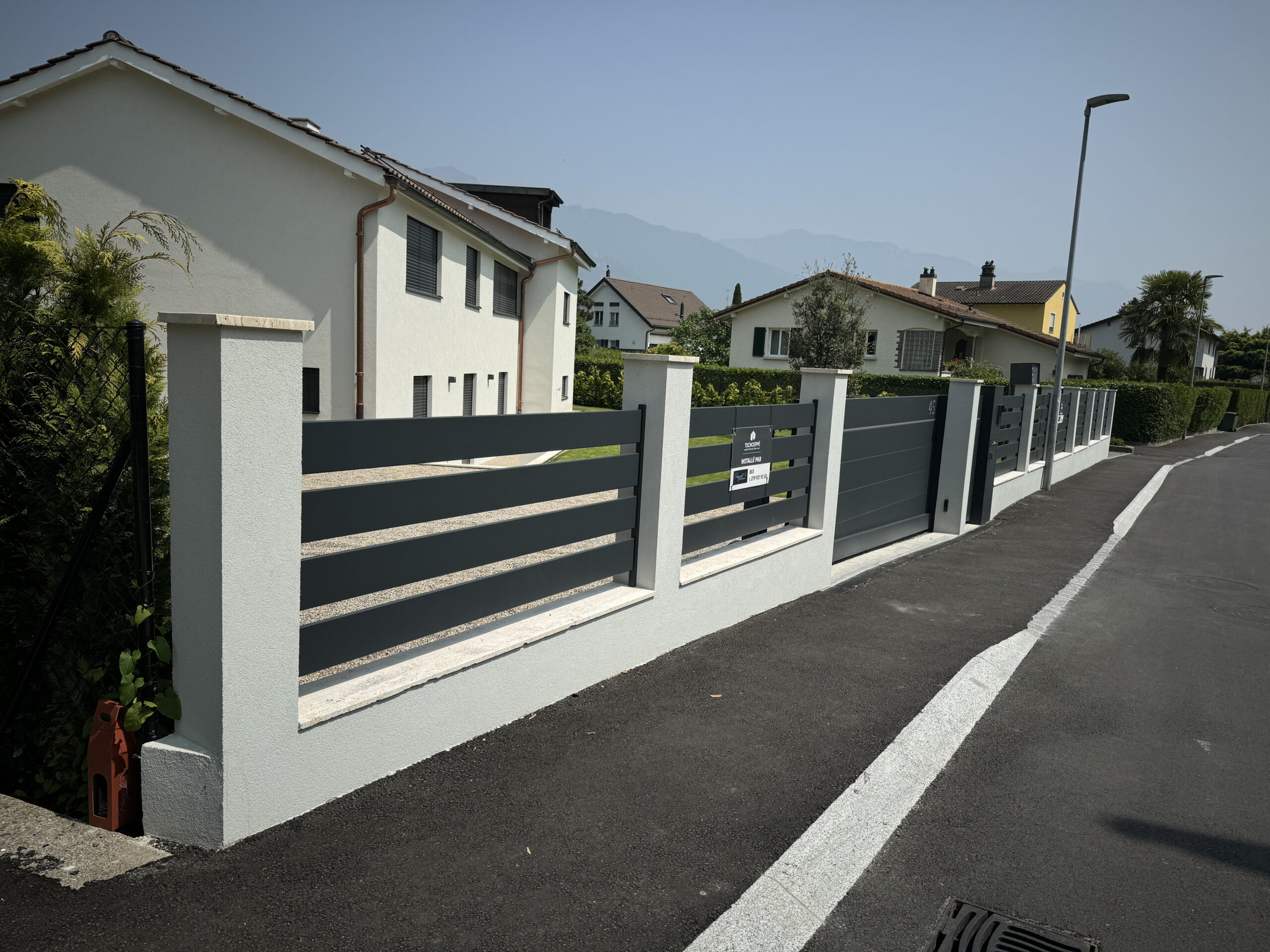 Clôture moderne grise et maison blanche, installation portail extérieur Suisse.