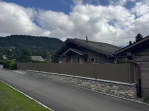Chalet bois, toit incliné, portail automatique et clôture installés par experts suisses en ouvertures extérieures entouré de montagnes.