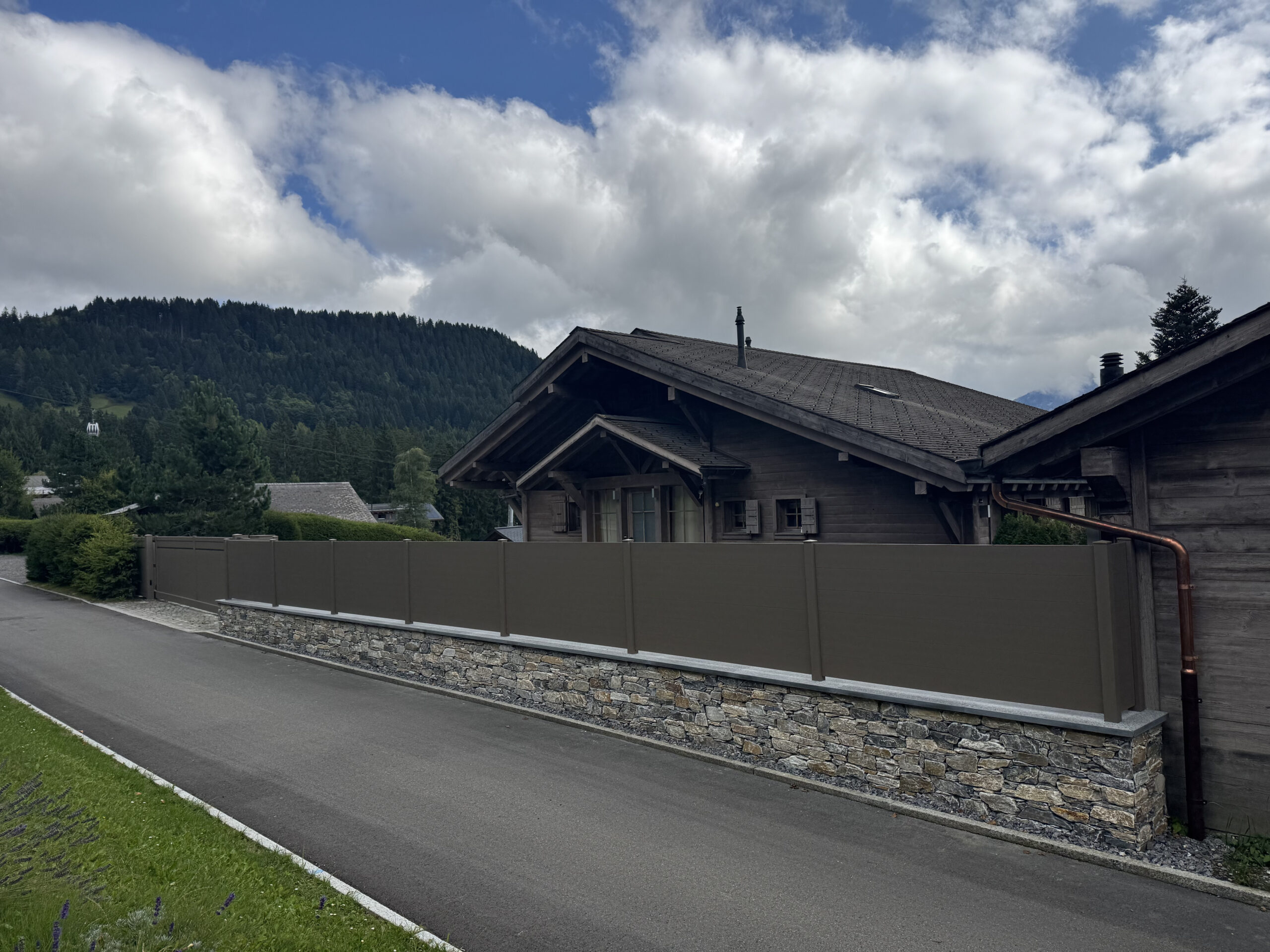 Chalet bois, toit incliné, portail automatique et clôture installés par experts suisses en ouvertures extérieures entouré de montagnes.
