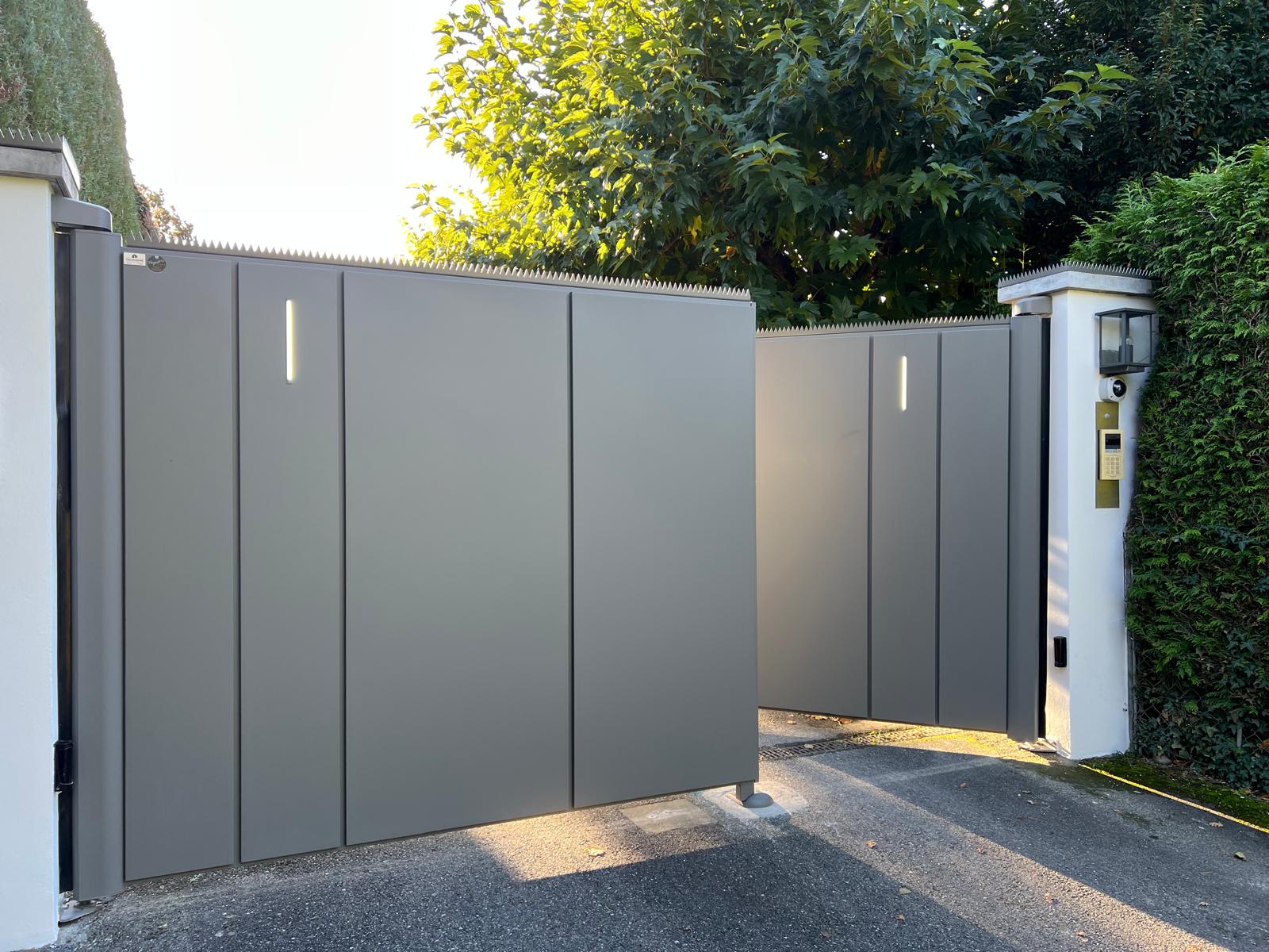 Portail métallique gris moderne installé avec piliers blancs, interphone, éclairage. Idéal extérieurs suisses professionnels qualité premium.