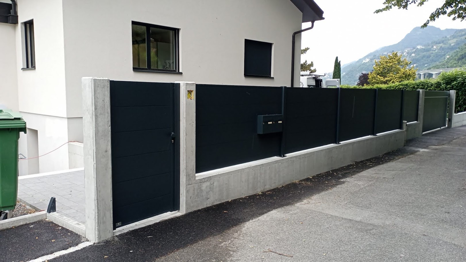 Maison moderne avec portail extérieur design, clôture métal-béton, paysage suisse verdoyant. Spécialiste ouvertures extérieures de qualité.