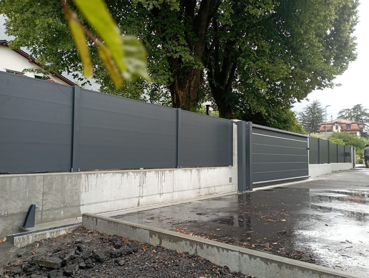Installation professionnelle de portail coulissant gris, clôture moderne, fond urbain et végétation en Suisse par spécialistes extérieurs.