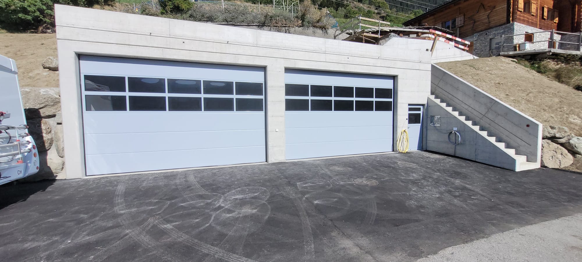 Installation portes de garage blanches vitrées, bâtiment béton, accès sécurisé Suisse.
