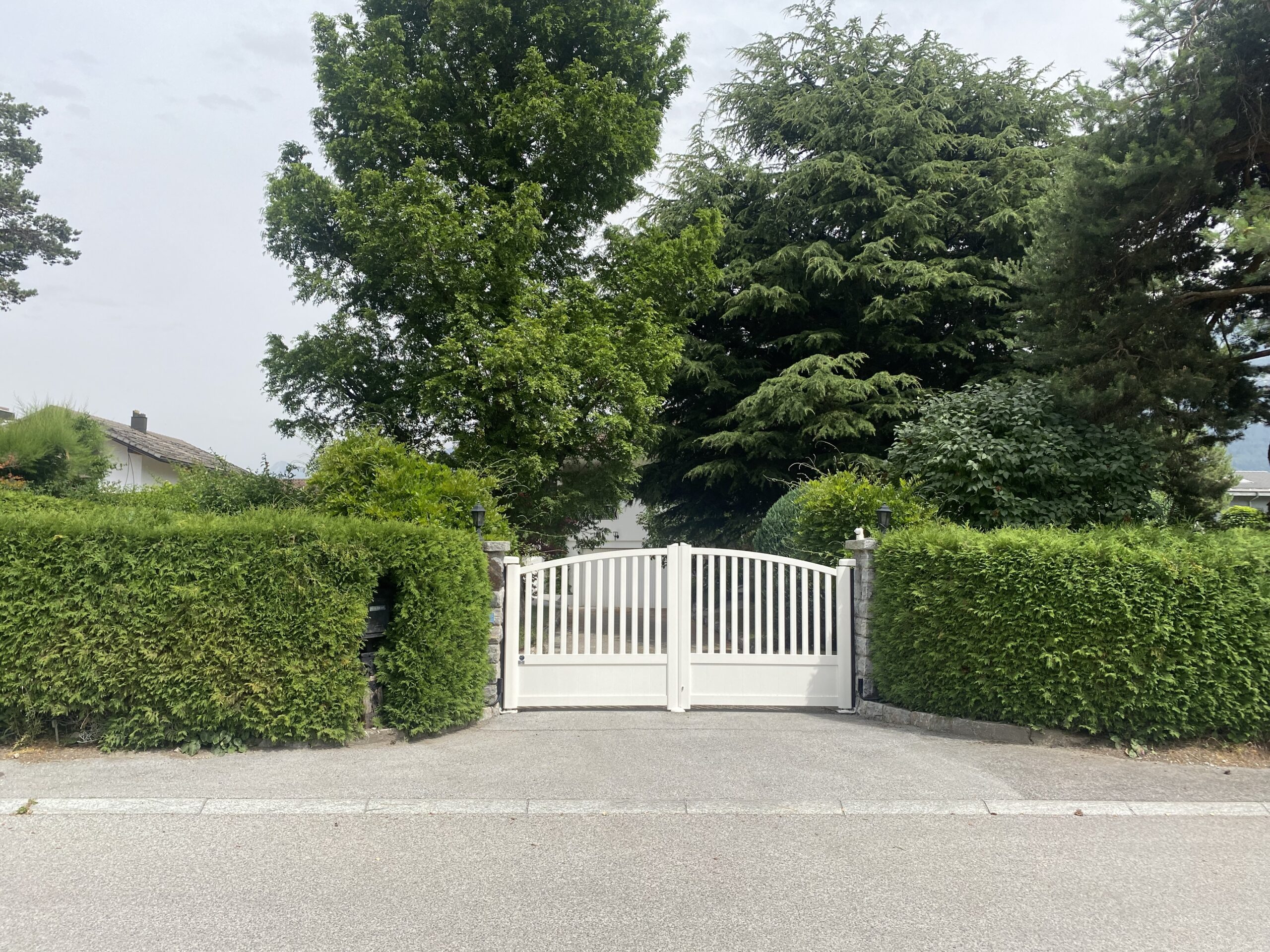 Portail blanc double, installation professionnelle, intégré haie verte, entrée résidentielle Suisse.